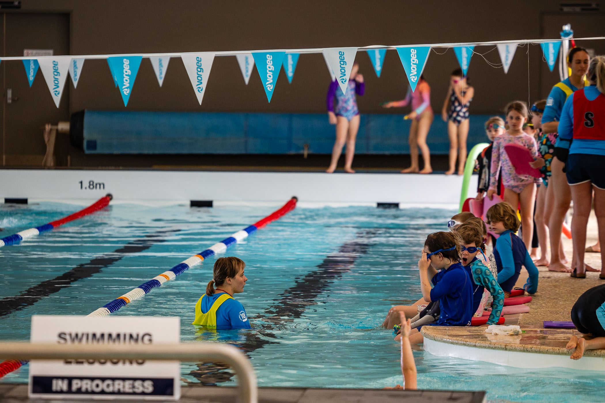 Children standing around the edge of Margaret River swimming pool. The swimming instructor is in the water.