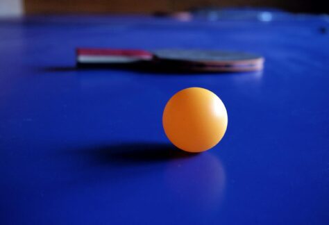 Vibrant orange ping pong ball with a table tennis racket on a blue table, emphasizing sport and leisure.